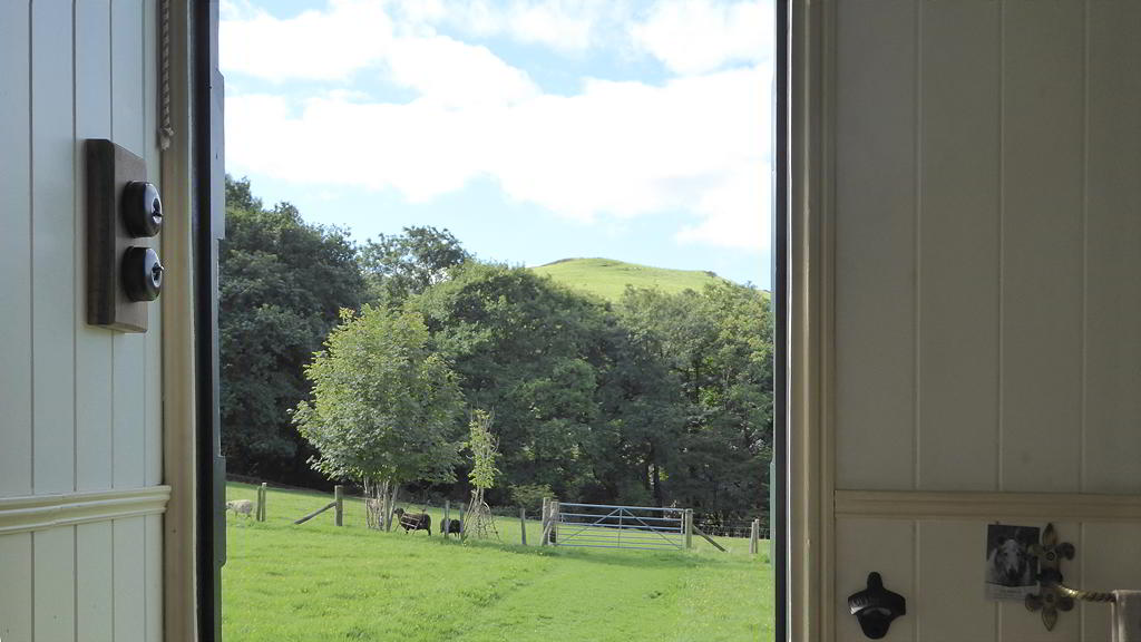 View though the doorway of sheep and hillside from inside the Hygge Hut